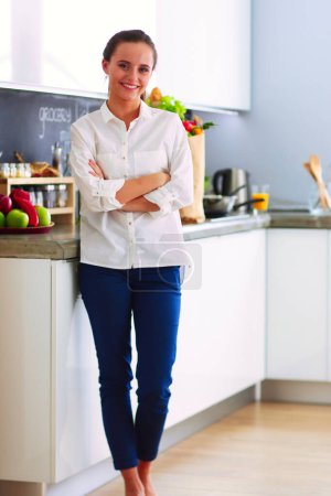 Téléchargez les photos : Portrait de jeune femme debout avec les bras croisés sur fond de cuisine. Femme dans la cuisine - en image libre de droit