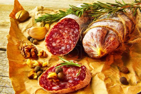 Photo for Italian salami wih sea salt, rosemary, garlic and nuts on paper. Rustic style. Close up. - Royalty Free Image