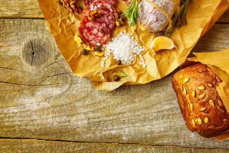 Photo for Italian salami wih sea salt, rosemary, garlic and nuts on paper. Rustic style. Close up. - Royalty Free Image