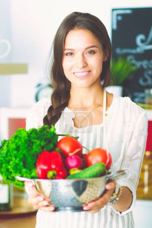 Téléchargez les photos : Jeune femme souriante tenant des légumes debout dans la cuisine. Jeune femme souriante. - en image libre de droit