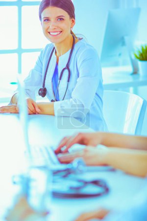 Téléchargez les photos : Médecin souriant utilisant un ordinateur portable travaillant avec ses collègues dans une chambre d'hôpital lumineuse - en image libre de droit