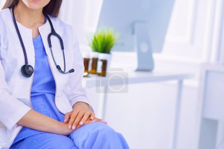 Photo for Beautiful female doctor sitting in a consulting room, smiling at the camera - Royalty Free Image