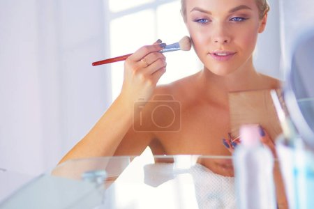 Photo for A picture of a young woman applying face powder in the bathroom. - Royalty Free Image
