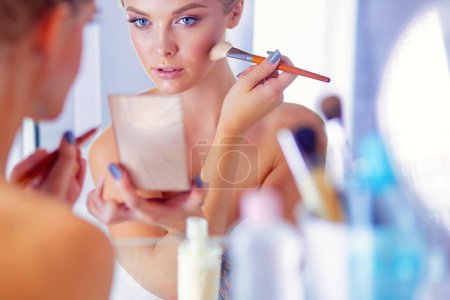 Téléchargez les photos : Une photo d'une jeune femme appliquant de la poudre visage dans la salle de bain. - en image libre de droit