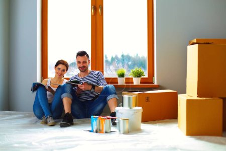 Téléchargez les photos : Couple attrayant assis sur le sol de la maison regardant jurnal et souriant à l'autre
. - en image libre de droit