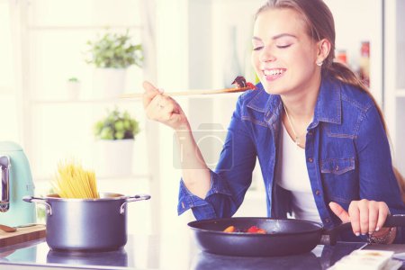 Photo for Young woman cooking healthy food holding a pan with vegetables is it. Healthy lifestyle, cooking at home concept. - Royalty Free Image