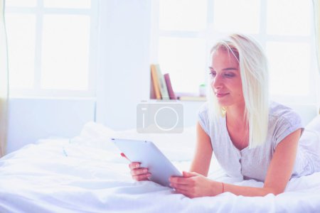 Foto de Chica sosteniendo tableta digital con pantalla en blanco y sonriendo a la cámara en el dormitorio
. - Imagen libre de derechos