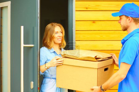 Photo for Smiling delivery man in blue uniform delivering parcel box to recipient - courier service concept. Smiling delivery man in blue uniform. - Royalty Free Image