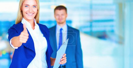 Photo for Portrait of young businesswoman showing ok in office with colleagues in the background. - Royalty Free Image