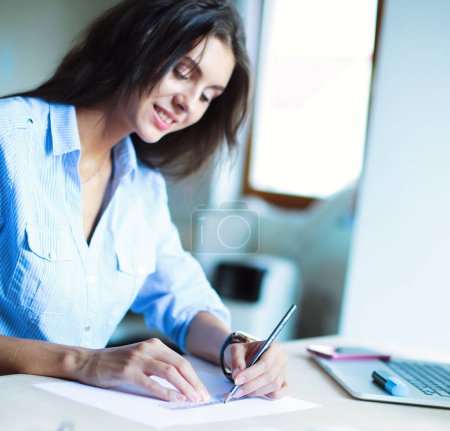 Foto de Mujer joven sentada en la mesa de la oficina, mirando la pantalla del ordenador portátil
 . - Imagen libre de derechos