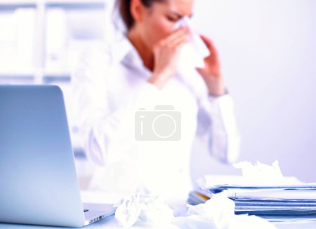 Téléchargez les photos : Portrait de la jeune femme malade triste qui s'assoit dans le bureau et essuie un nez avec une serviette
. - en image libre de droit