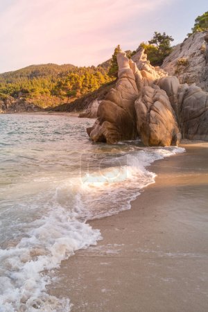 Vourvourou, Chalkidiki oder Chalkidiki, Griechenland Sommer-Sonnenuntergang mit türkisfarbenem Meer, waldgrünen Bergen und Felsen am Fava Sandstrand