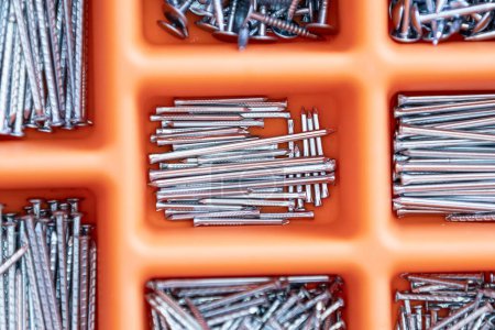 Photo for Collection of nails, thumb nails, screws, plastic and bolts in plastic box on the wooden table - Royalty Free Image