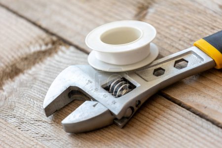 Photo for Different plumbing spare parts, white sealing tape and adjustable wrench on wooden background. Close-up - Royalty Free Image