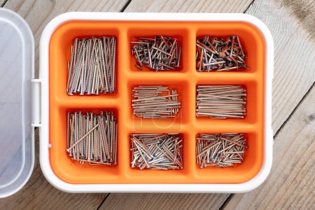 Collection of nails, thumb nails, screws, plastic and bolts in plastic box on the wooden table