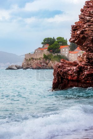 Hotel en la isla de Sveti Stefan al atardecer, cerca de Budva, Montenegro. Olas y rocas rojas