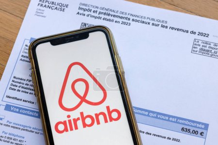 Foto de París, Francia - 30 de noviembre de 2023: Logo de Airbnb en un smartphone en un recibo de impuestos. El gobierno francés quiere gravar más los alquileres a corto plazo. - Imagen libre de derechos