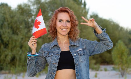 Téléchargez les photos : Joyeux jeune femme avec le drapeau du Canada debout sur fond de nature. - en image libre de droit