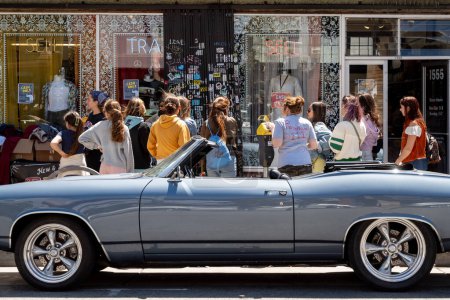 Photo for Haight Ashbury Street, San Francisco, California, USA - April 22, 2023: Back view of crowd of female consumers waiting while standing near car in front of retail sales shop with sign in sunny daylight - Royalty Free Image
