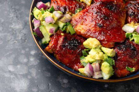 Lemon and tomato paste glazed Mediterranean style chicken thighs served with avocado and cucumber salsa, low carb keto meal concept.