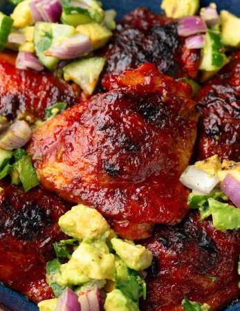 Lemon and tomato paste glazed Mediterranean style chicken thighs served with avocado and cucumber salsa, low carb keto meal concept.