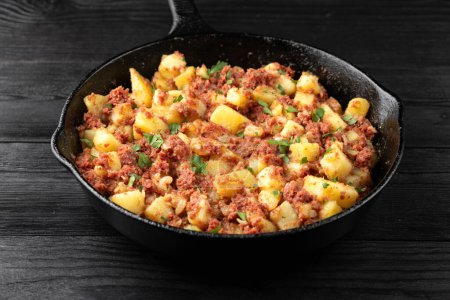 Corned beef hash with potatoes in iron cast pan.
