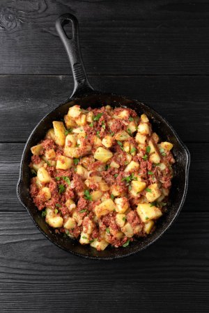 Corned beef hash with potatoes in iron cast pan.