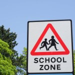 A road sign in the UK showing a graphic of children in a red triangle to alert motorists that the area is a school zone