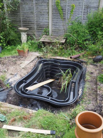 Ein schwarzer, starr vorgeformter, rechteckiger Teich, der frisch in einem Garten angelegt wurde