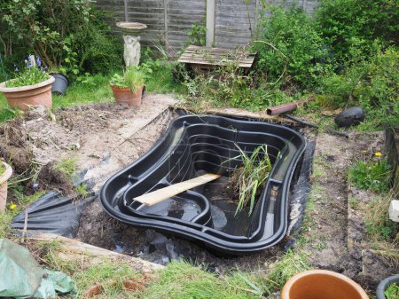 Ein schwarzer, starr vorgeformter, rechteckiger Teich, der frisch in einem Garten angelegt wurde