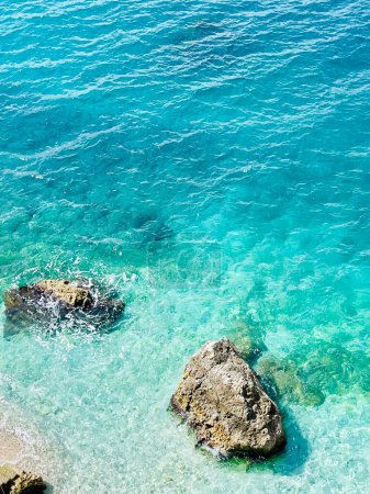 Rocky beach and crystal turquoise water of Ionian Sea in Albania. Calm and relaxing view with flowers. summer holidays concept background. Copy space. Vertical photo. 
