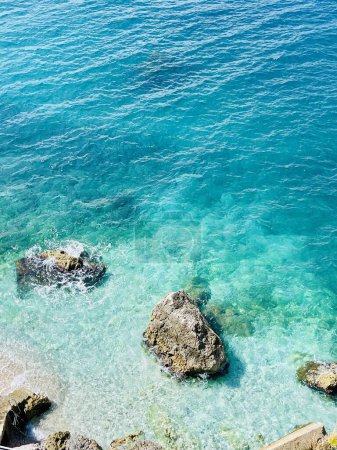 Photo for Rocky beach and crystal turquoise water of Ionian Sea in Albania. Calm and relaxing view with flowers. summer holidays concept background. Copy space. Vertical photo. - Royalty Free Image