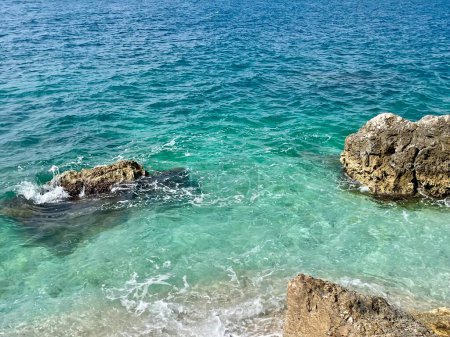 Rocky beach and crystal turquoise water of Ionian Sea in Albania. Calm and relaxing view with flowers. summer holidays concept background. Copy space. Horizontal photo. 