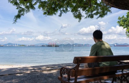 Vista trasera del hombre sentado en el banco mirando al océano en verano