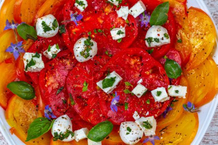 Photo for Tomatoes cut into slices with borage flowers with small cubes of Feta and basil leaves. - Royalty Free Image