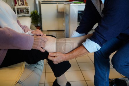 Téléchargez les photos : Infirmière freelance lors d'une visite quotidienne à une patiente pour des soins sur ses jambes et l'installation de chaussettes de compression. - en image libre de droit
