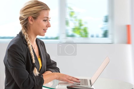 Photo for Young blonde woman in profile with her hands on the computer keyboard. - Royalty Free Image
