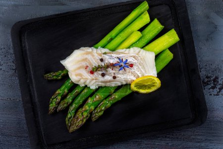 Cod steak placed on green asparagus resting on a black board.