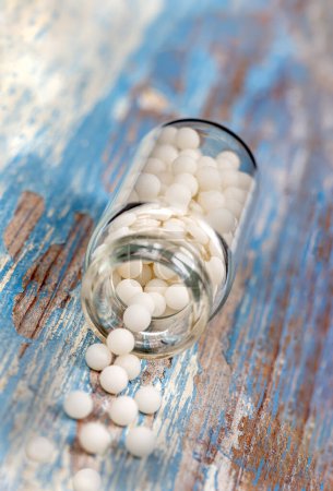 Foto de Homeopatía: primer plano de los gránulos derramados entre pequeñas flores sobre un fondo claro. - Imagen libre de derechos