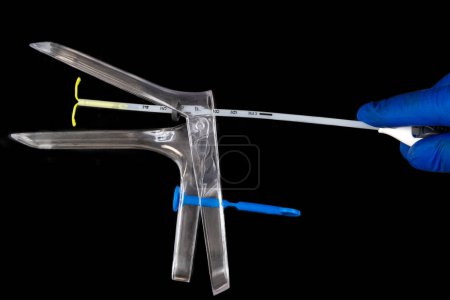 The IUD enters the uterus using the speculum - Tight shot on black background.
