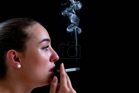 Foto de Primer plano de una mujer fumando un cigarrillo sobre un fondo negro, creando humo ondulante. - Imagen libre de derechos