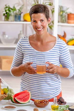 Frau, eine Tasse Tee in der Hand, umgeben von Getreide, frischen Früchten und Trockenfrüchten, Honig,