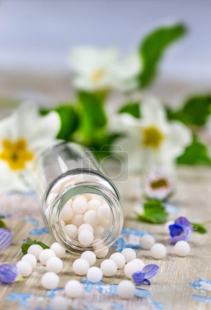 Homeopathy : close-up of homeopathic granules spilling out among small flowers on a light background.