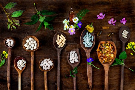 Naturmedizin-Kapseln, versteckt, Ampulle und Heilpflanzen von oben gesehen, in Holzlöffeln.