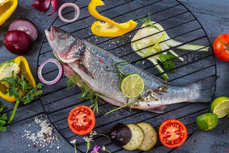 Sea bass placed on a barbecue grill surrounded by vegetables, before cooking.