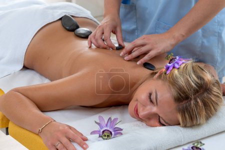 Photo for Top view - The masseur positions the basalt pebbles in the center of the patient's back - Royalty Free Image