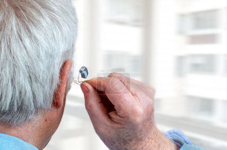 Foto de Foto americana de colocar un audífono a un anciano de pelo blanco, vista trasera. - Imagen libre de derechos