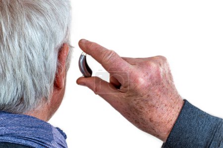 Photo for American shot of fitting a hearing aid to a white-haired senior citizen, rear view. - Royalty Free Image