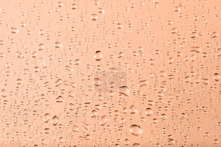Metallic foil texture with water drops in trendy color 2024 Peach Fuzz as background with copy space