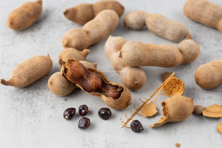 Ripe whole and shelled tamarind fruits  with seeds closeup on stone background. Healthy exotic food.